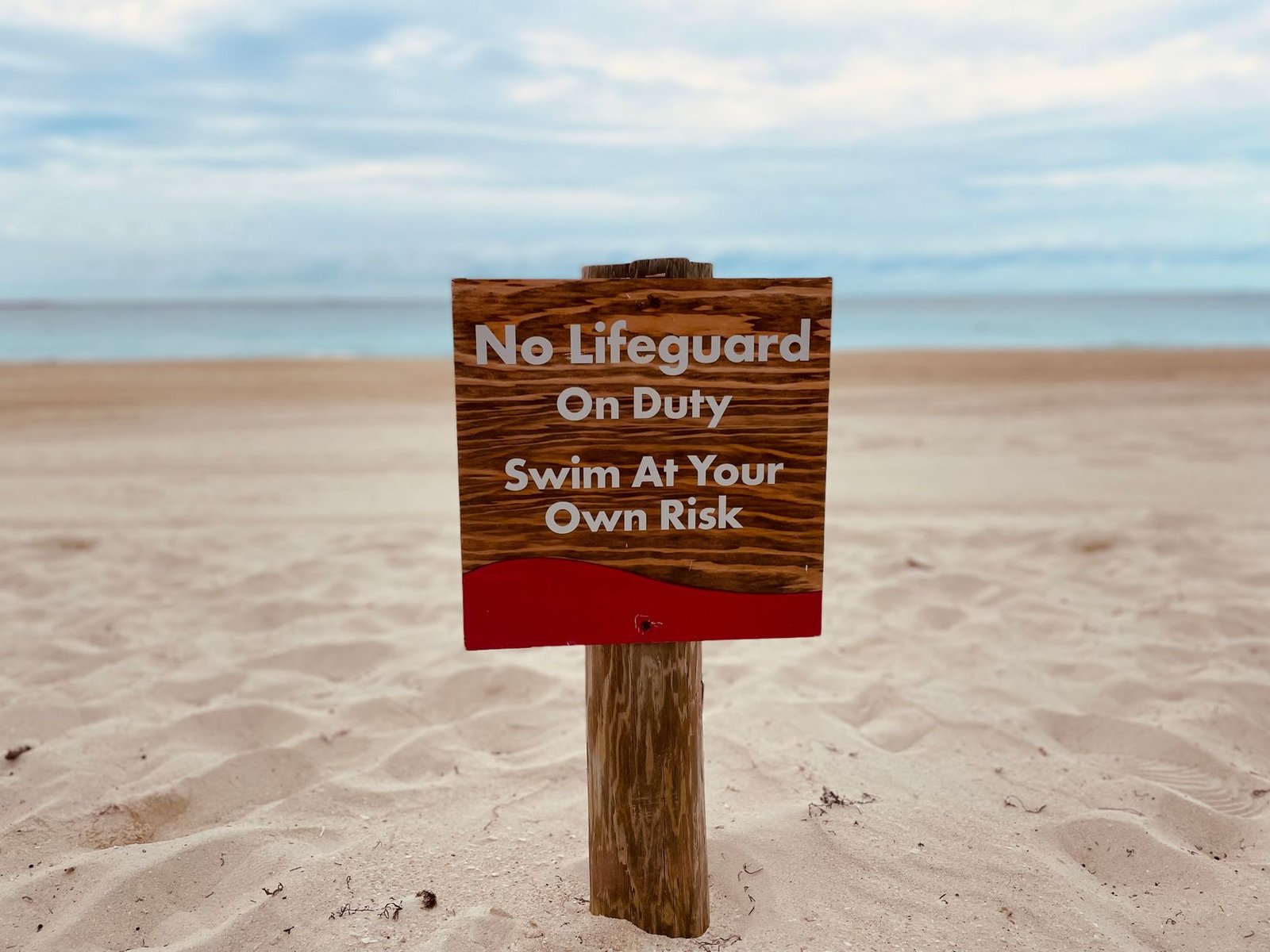 A sandy beach with a no lifeguard warning sign