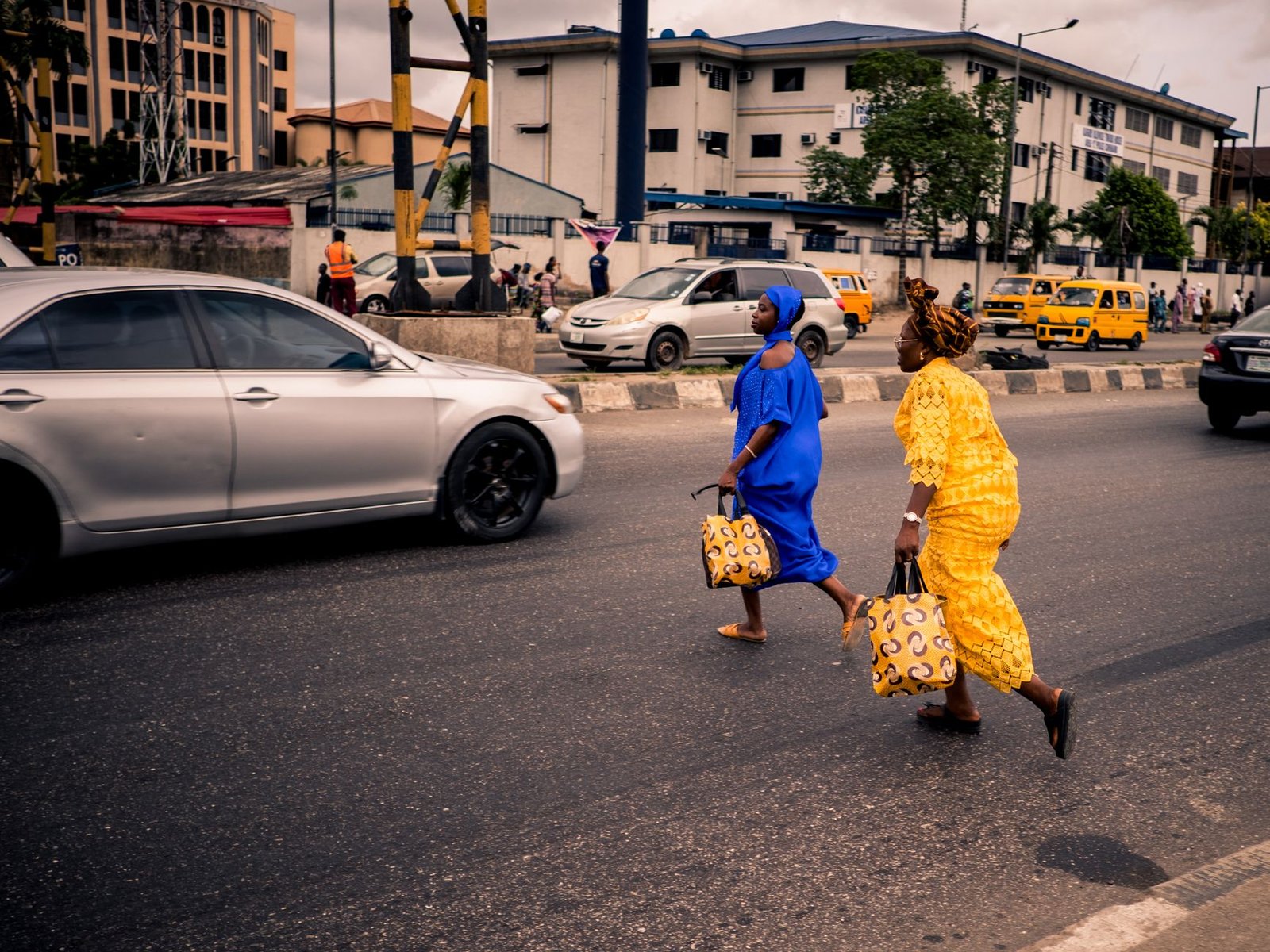 Two women in traditional Nigerian outfits cross a bustling street in Lagos, Nigeria