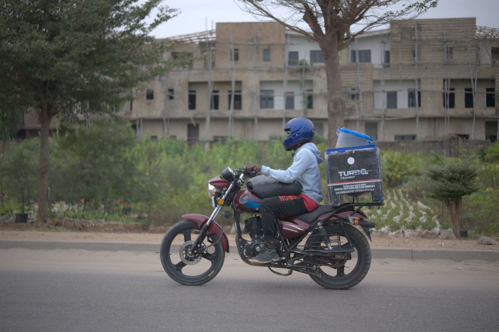 Motorcycle delivery rider with package box in urban Nigeria setting.