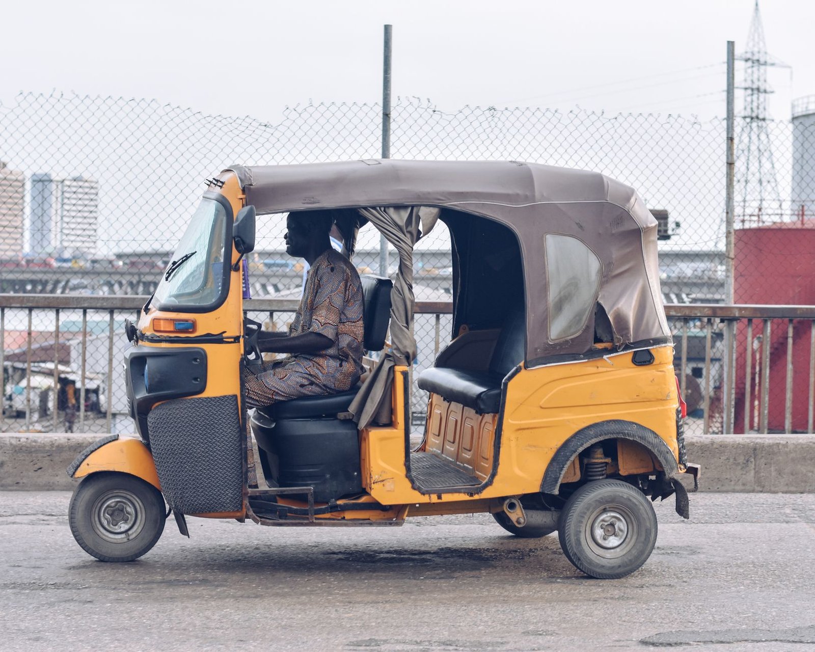 A yellow tricycle taxi navigates a Lagos street, capturing urban life and local transportation.