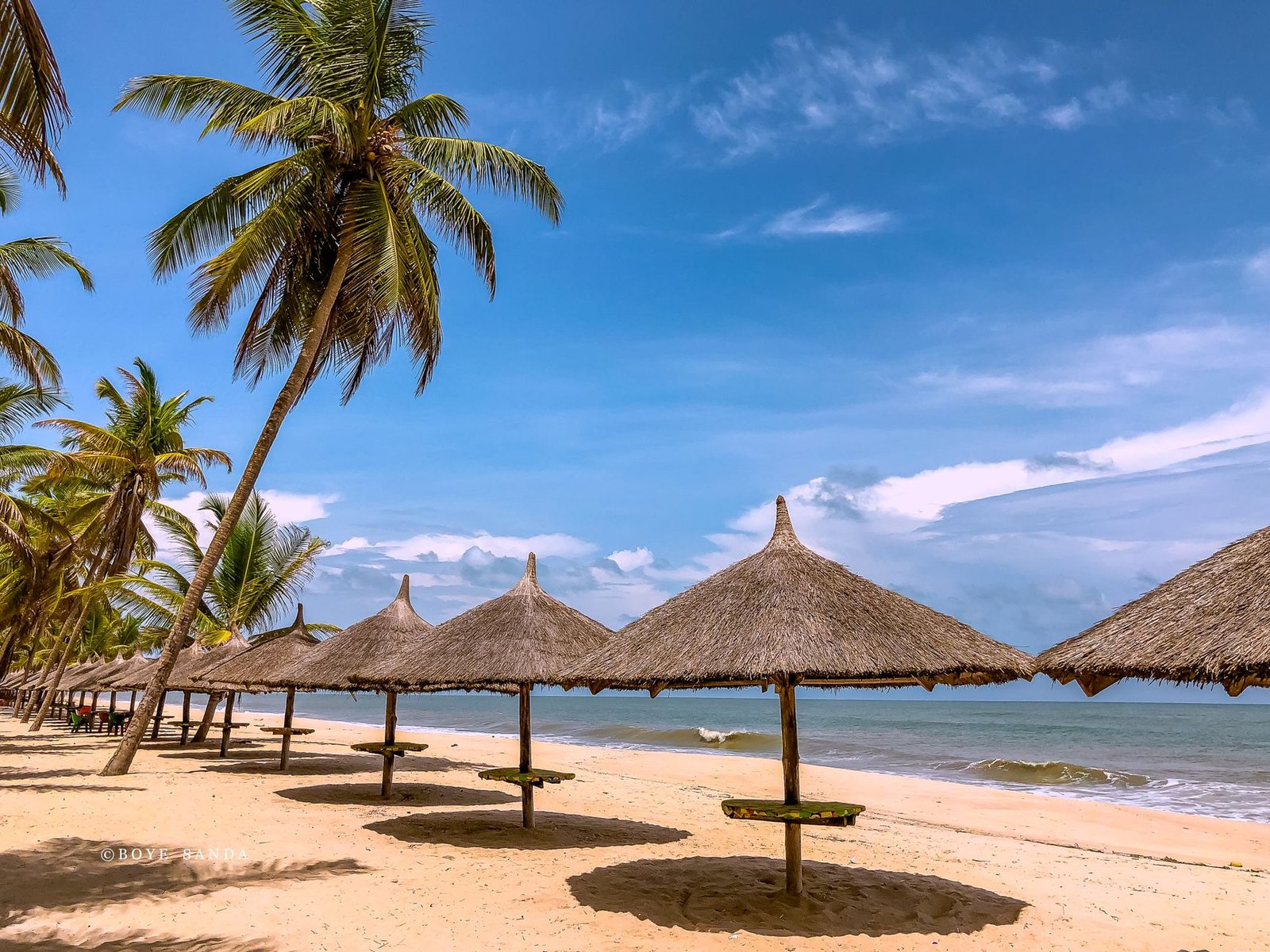 Scenic tropical beach in Lagos, Nigeria with palm trees and thatched sun umbrellas.