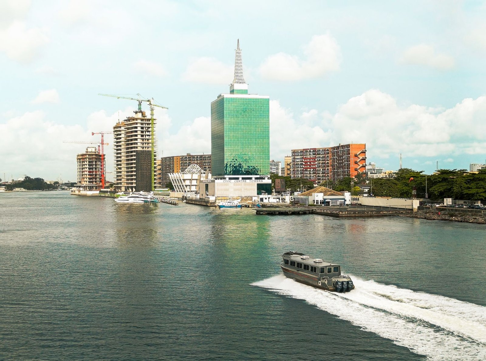 Scenic view of Lagos skyline featuring modern buildings and a motorboat in the lagoon under a bright sky.