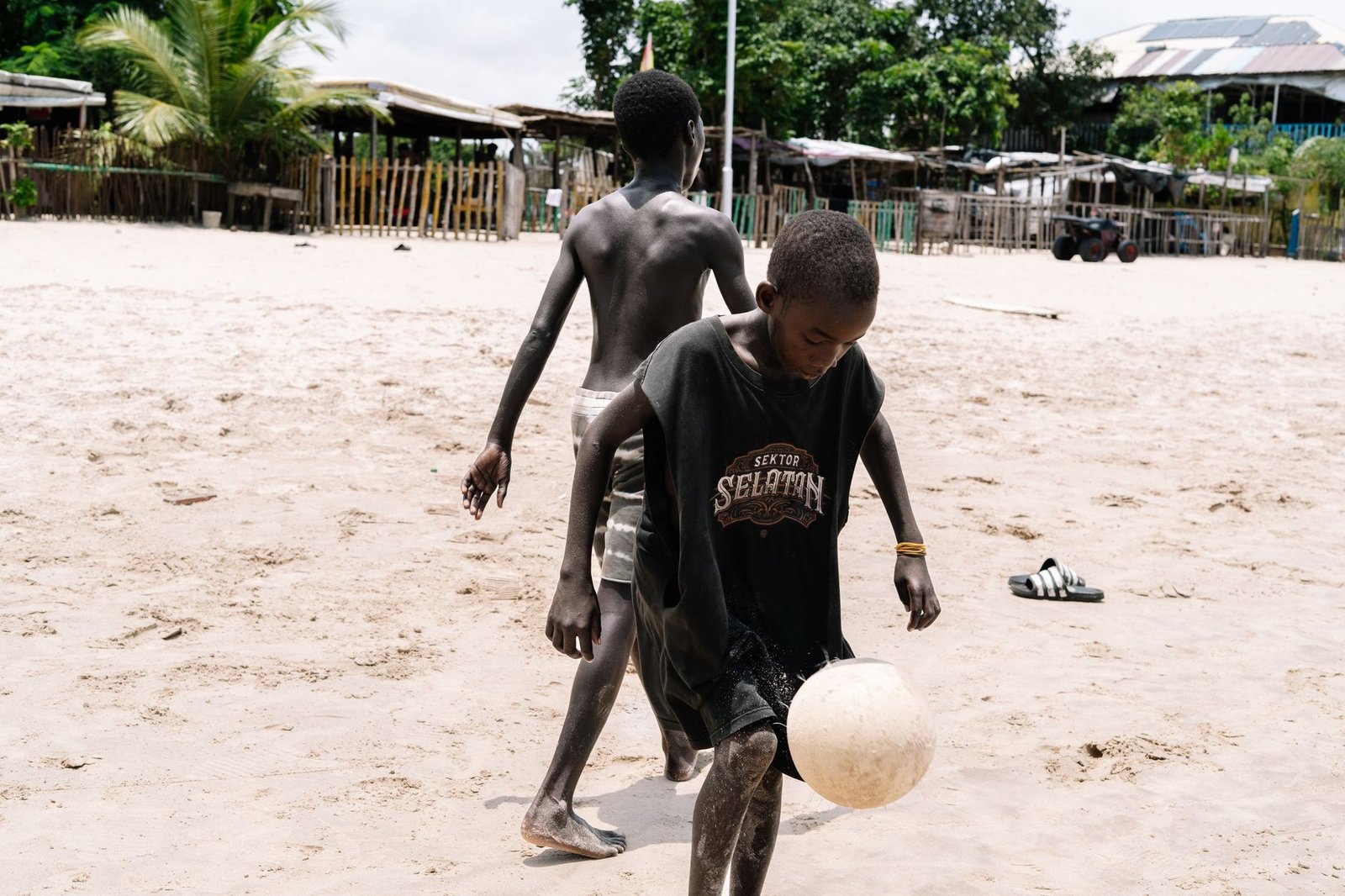 Two boys playing soccer on a sandy Lagos beach under the sun.