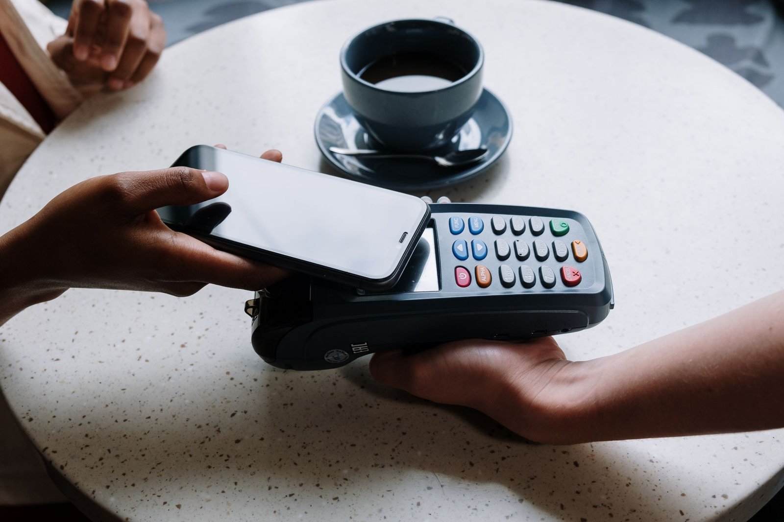 Person making a contactless payment with a card reader on a cafe table.