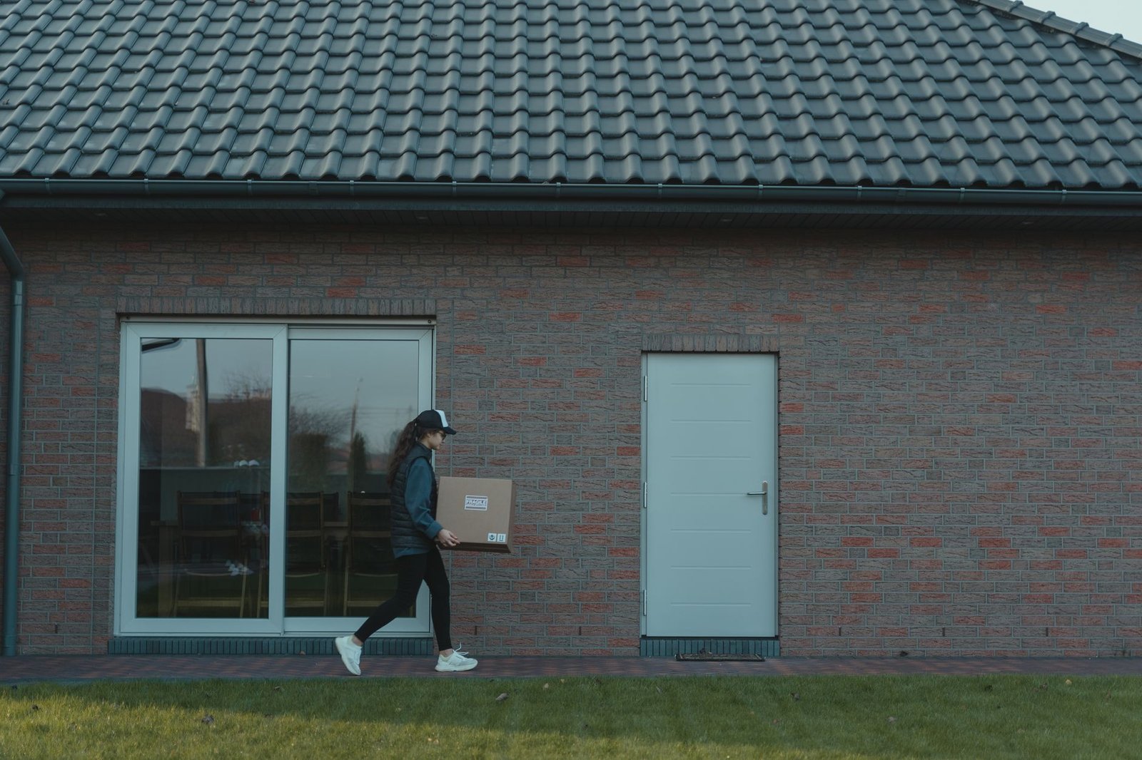 A courier delivers a package to a modern brick house, showcasing logistics in action.
