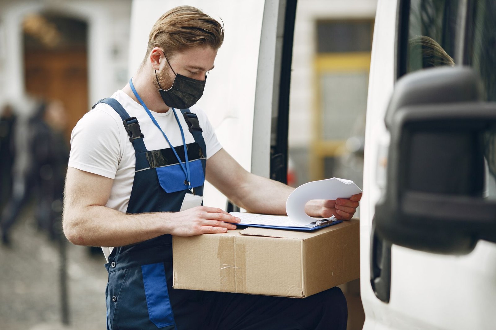 A delivery worker wearing a face mask checks a package next to a van