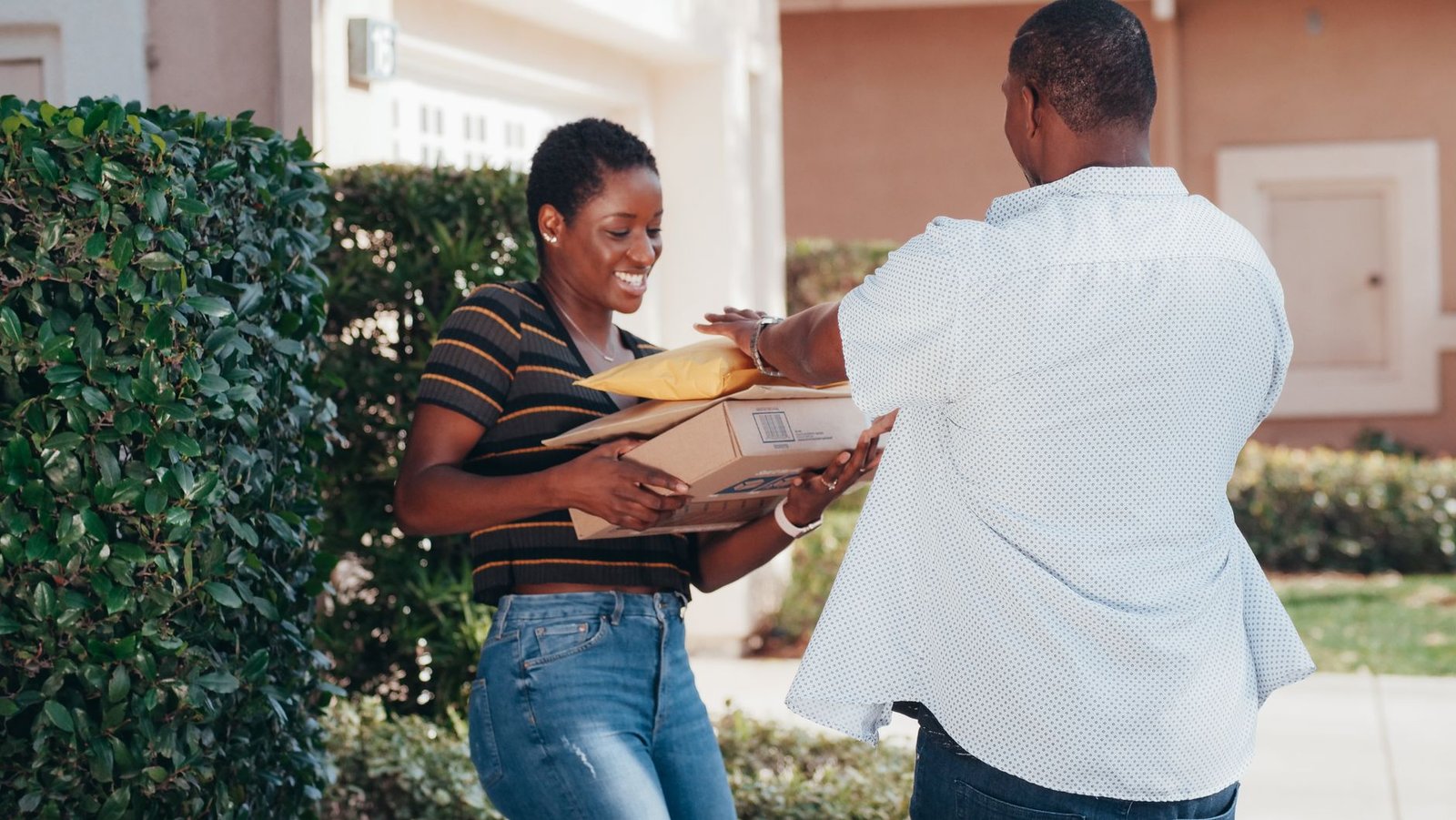 A smiling woman receives multiple packages from a delivery man outdoors