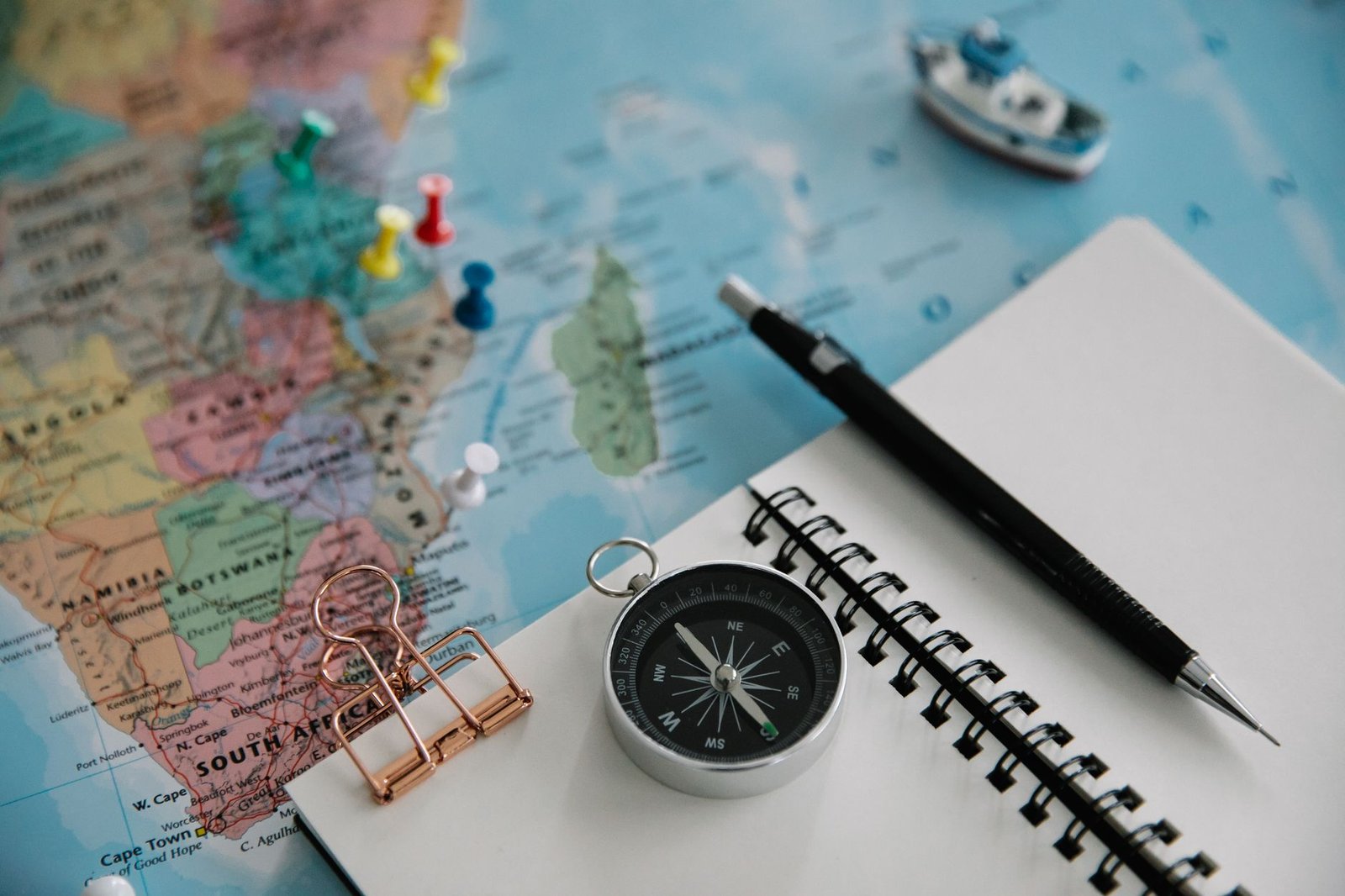 Flat lay of travel planning tools including a map, compass, notebook, and pen