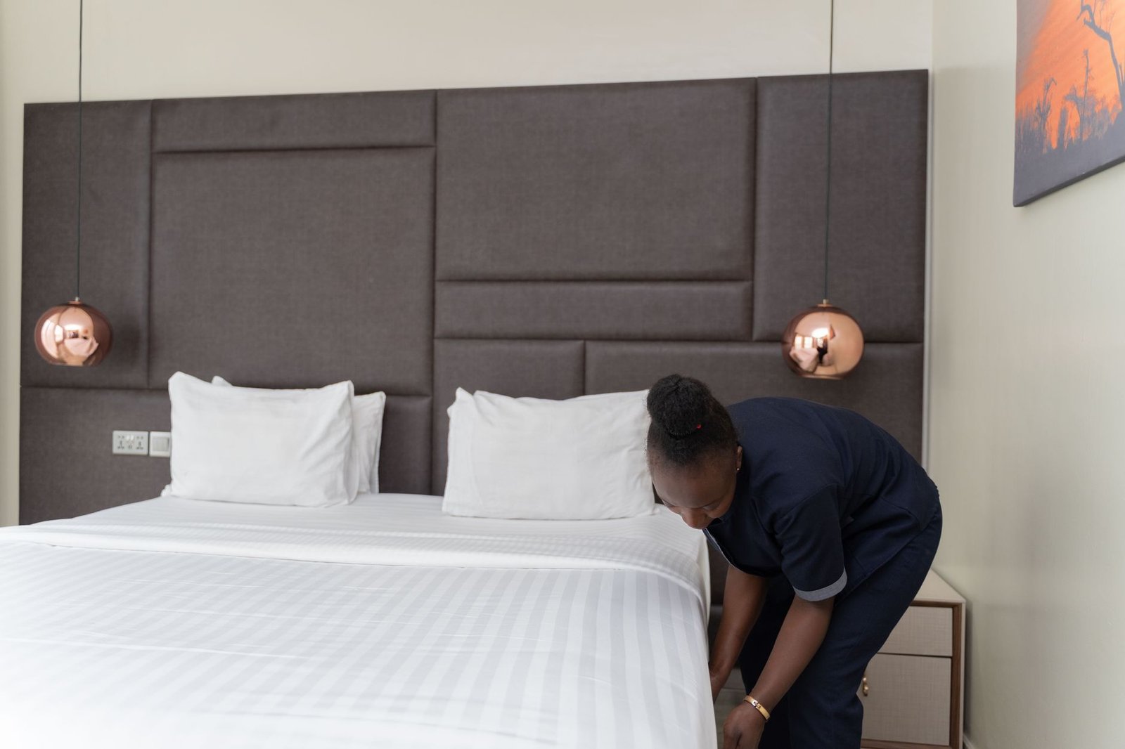 Hotel staff member prepares a bed in a modern hotel room