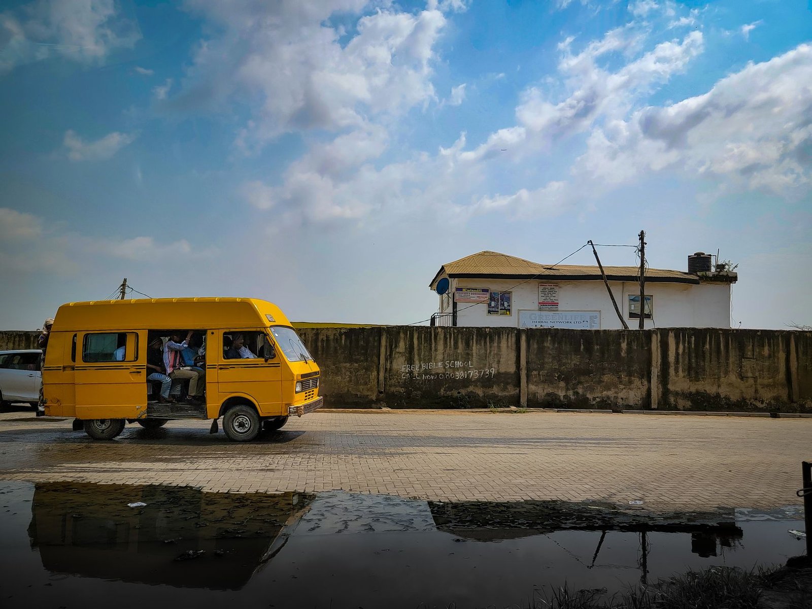 Yellow bus driving on a street in Nigeria with cloudy sky above, depicting urban transport