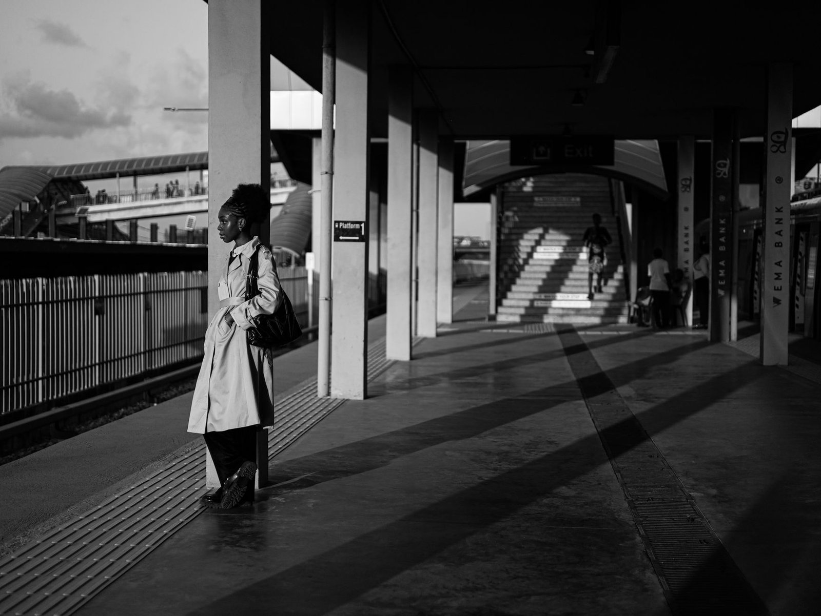 Artistic black and white photo of a woman waiting at a Lagos train station, showcasing urban life